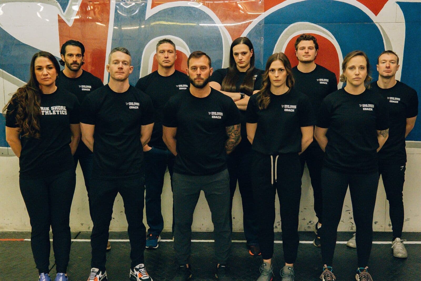 The Erie Shore Athletics coaching team in front of the gym mural